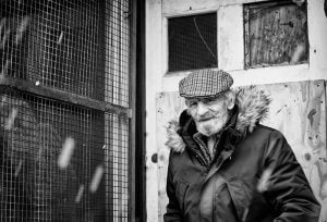 Street photography: An old man photographed in black and white standing in front of a building.