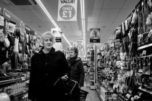 Black and white street photography of a woman walking down a supermarket aisle.