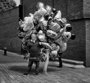 Street photography of a man surrounded by balloons.