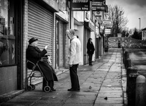 A street photography capturing a woman in a walker and a man in a wheelchair.