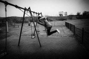 A black and white street photography capturing a boy swinging on a swing.