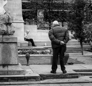 Street photographer capturing a man observing a statue from a bench.