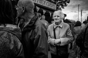 Black and white street photography of an older woman standing in a crowd.
