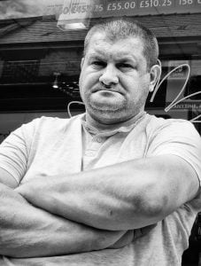 A man with his arms crossed in front of a shop.