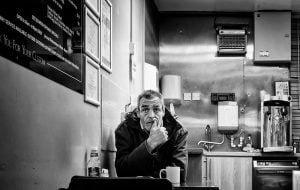 A man peacefully sits at a table in a street café, sipping on his coffee.