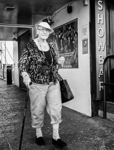 Street photography of a woman with a cane walking down the street.