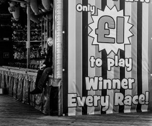 A street photography masterpiece capturing a man on a bench at a carnival in black and white.