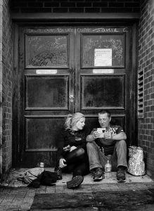 Monochrome street photography featuring a couple seated in front of a doorway.