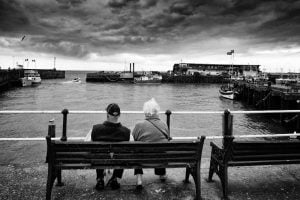 Two people sitting on a coastal bench.