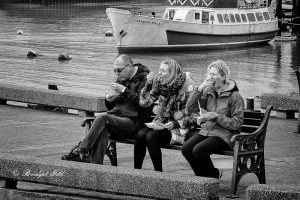 Street photography of three people sitting on a bench.