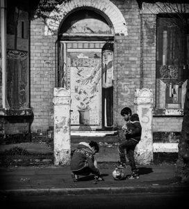 Street photography of two boys playing soccer in front of an old building.