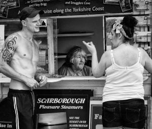 Street photography of a woman engaging in conversation with a man at a food stand.