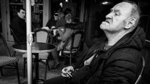 A black and white street photography capturing a man sitting at a table.