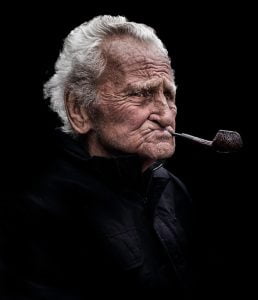 An old man smoking a pipe in street photography.