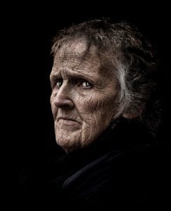 An old woman captured in street photography with a black background.