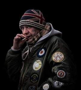 Street photographer captures man with British flag patch on hat talking on phone.