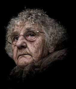 Street photography of an elderly woman donning glasses and fur attire against a black background.