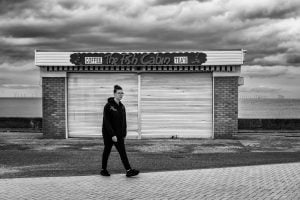 A monochrome street photograph featuring a man walking.