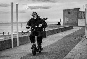 A man riding an electric scooter in Rhyl near the ocean.