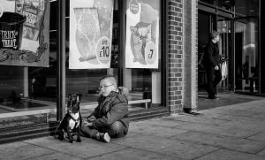 Street photography: A man capturing an image of a dog sitting on the sidewalk.