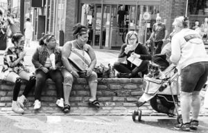 Street photography of people seated on a brick wall.