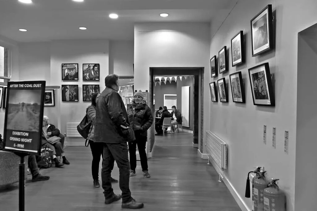 A black and white photo capturing people at an exhibition in a hallway.